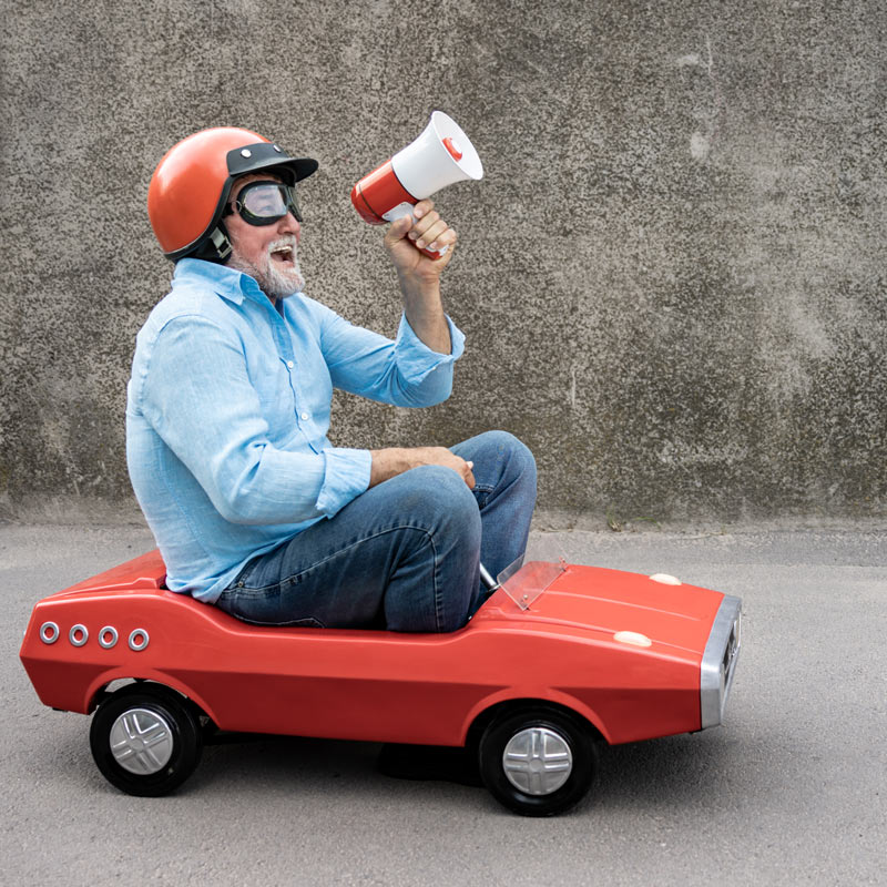 Senior man driving retro pedal car and fundraising loudspeaker